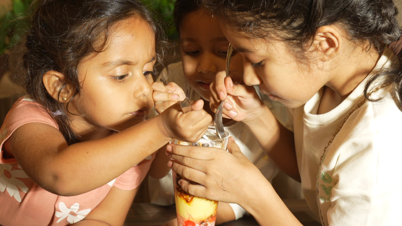 Three children happily sharing a tall sundae glass at Cravory